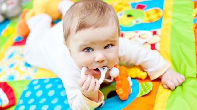 Un neonato che gioca sul tappeto colorato e morde il suo sonaglino Il sonaglio: un gioco attraverso il quale scoprire il mondo dei suoni