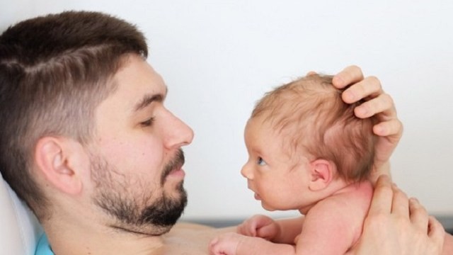 Un papà che tiene in braccio il suo neonato e lo accudisce Anche i papà accudiscono i loro bimbi
