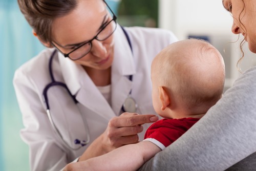 Dottoressa che controlla lo stato di salute del bambino in braccio alla mamma. Tosse, otite e influenza: come prevenirli in tre mosse