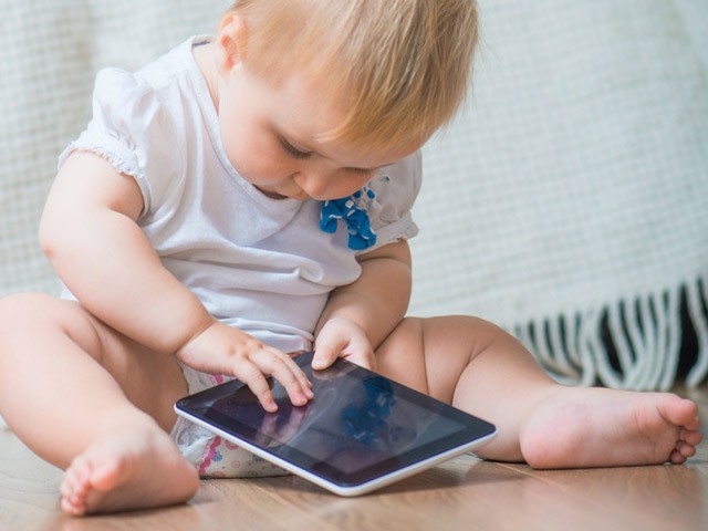 Neonato seduto che gioca con lo smartphone del suo genitore 75% dei bimbi utilizza lo smartphone, madri e padri troppo tolleranti