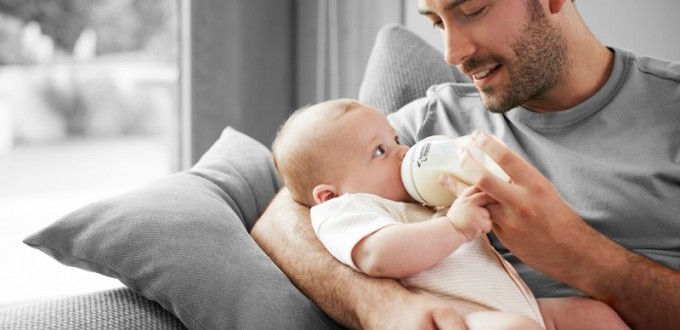 Un neo papà che tiene in braccio il suo neonato e lo allatta.
Un legame forte tra papà e neonato/a.
Come il neo papà si innamora del suo bambino/a