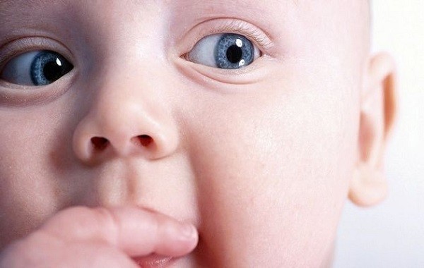 Piccolo neonato con gli occhi azzurri che porta la mano alla bocca. Neonato dagli occhi azzurri che ha la manina in bocca.